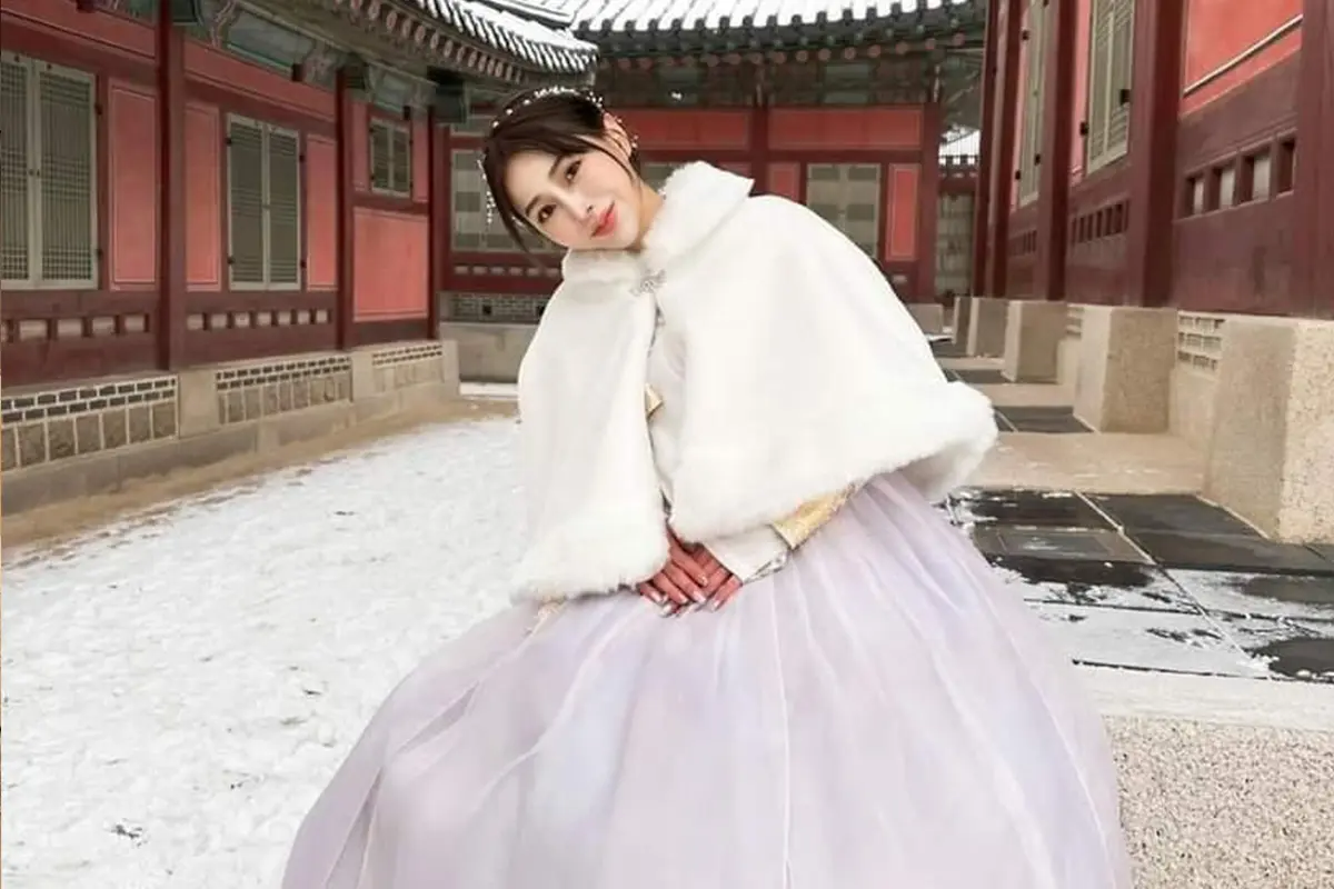 身穿傳統韓服的女士站在雪地上,背景是傳統韓國建築,展現冬日韓國的獨特美感.